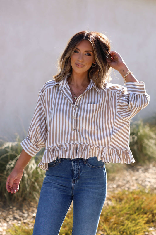 Woman outdoors in the Free People Neutral Bailey Stripe Shirt and blue jeans, smiling and touching her hair.
