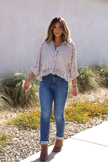 Woman in Free People Neutral Bailey Stripe Shirt stands outdoors near plants and rocks on a sunny day.