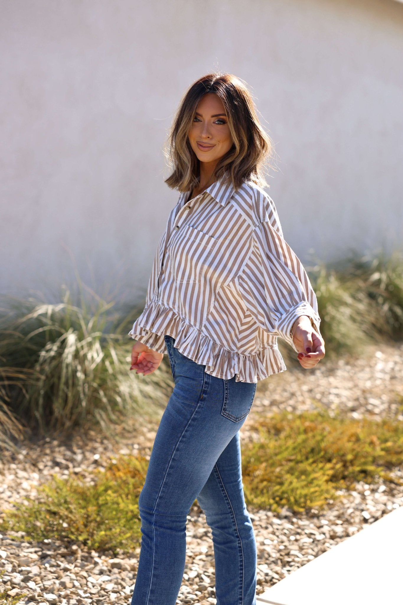 Woman with shoulder-length hair smiles outdoors in the Free People Neutral Bailey Stripe Shirt - FINAL SALE, styled with jeans.