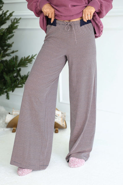 Person in Free People Peach Combo Out and About Pants, pink socks, and mauve sweatshirt stands by a Christmas tree indoors.