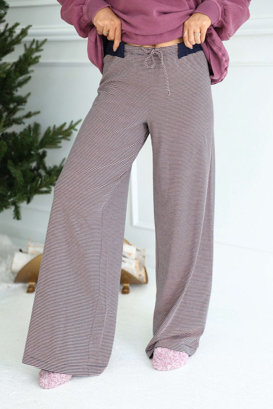 Person in Free People Peach Combo Out and About Pants, pink socks, and mauve sweatshirt stands by a Christmas tree indoors.