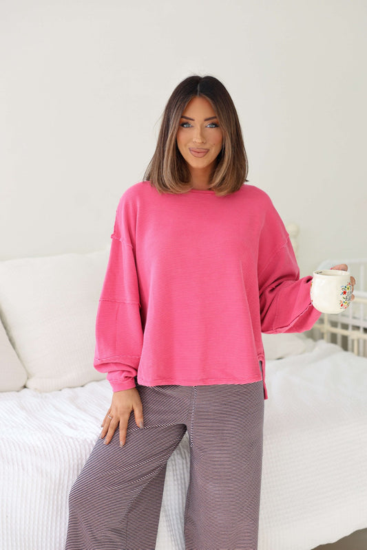 A woman in the Free People Pink Total Eclipse Top stands indoors, holding a white mug and smiling—effortlessly casual.