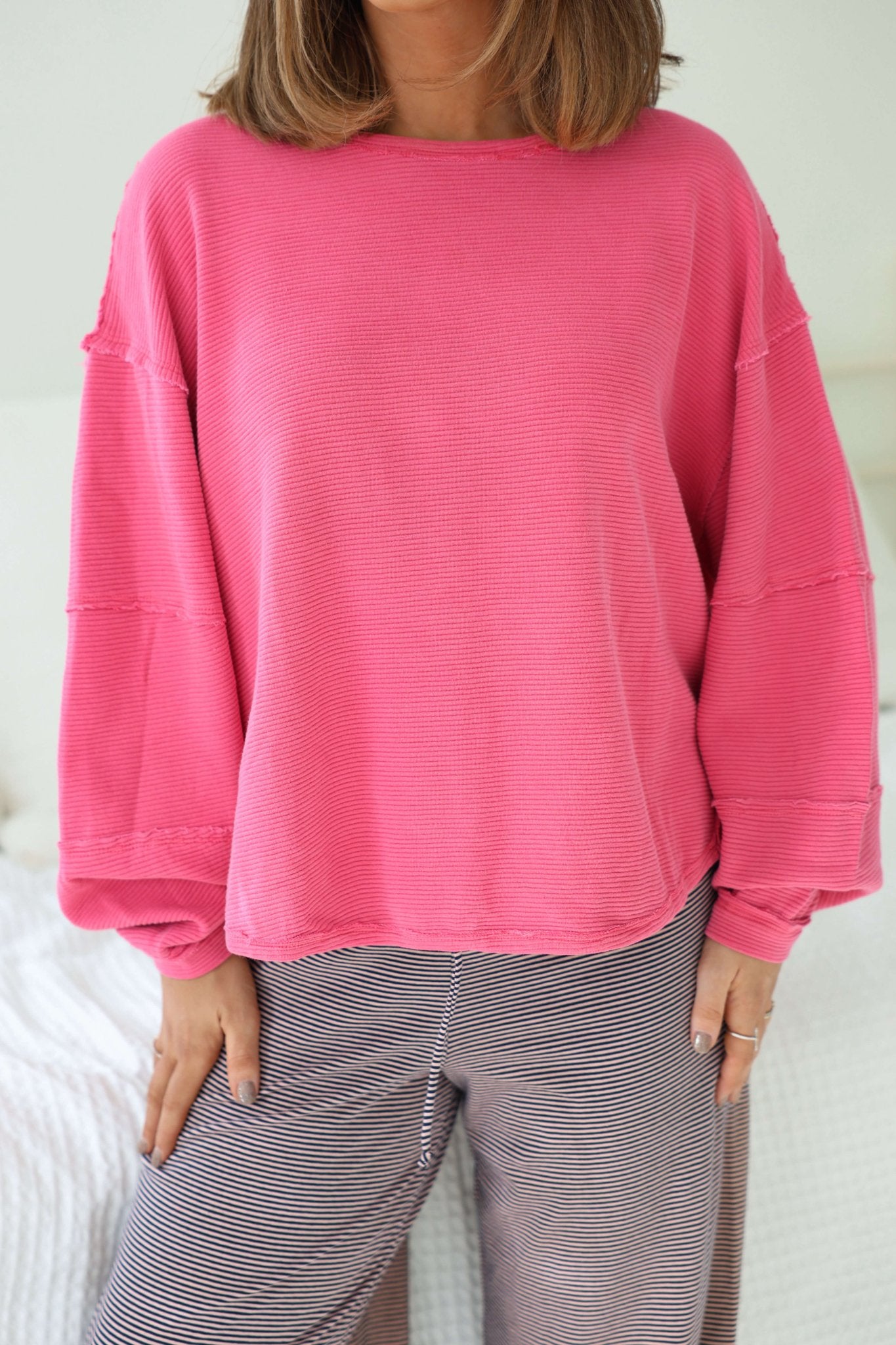 Person wearing a bright pink Free People Pink Total Eclipse Top and gray striped pants, standing indoors with hands by their sides.