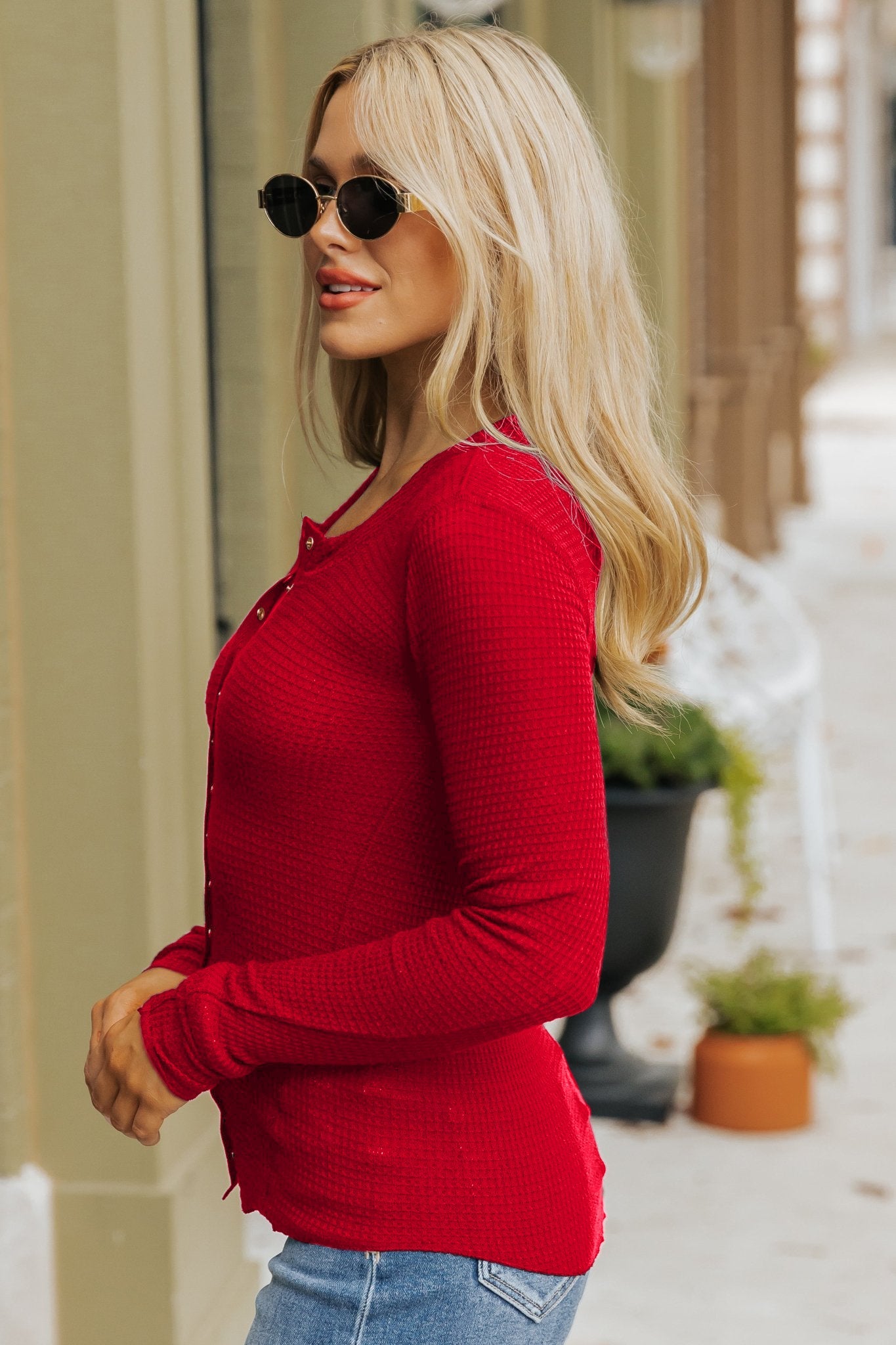 Woman with long blonde hair in sunglasses smiles outdoors wearing the Free People Red Going Places Cardigan and blue jeans.