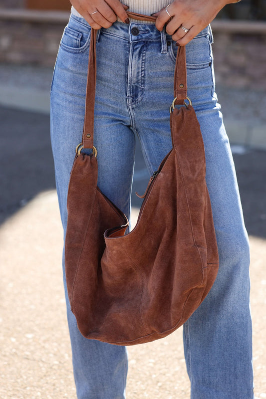 Person in blue jeans holding the Free People Rust Roma Suede Tote Bag by its straps.