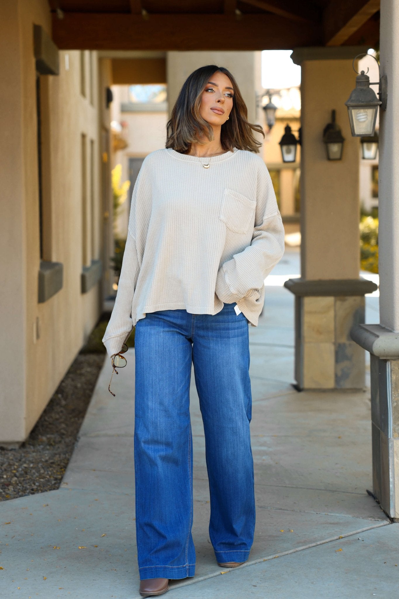 A woman stands confidently outside in the Free People Stone Dawson Pocket Thermal Top and wide-leg jeans.