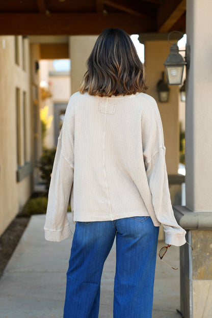 Someone in a Free People Stone Dawson Pocket Thermal Top and blue jeans stands outdoors holding sunglasses, facing away.