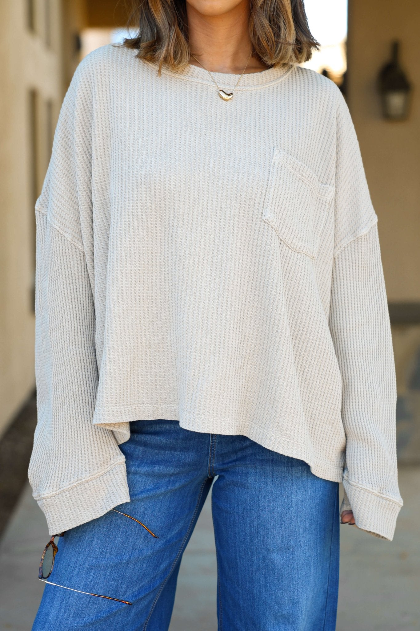 A woman in the Free People Stone Dawson Pocket Thermal Top, a loose beige sweater, pairs it with blue jeans outdoors.