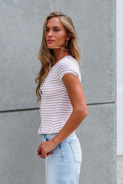 Woman with long hair wears the Free People Stripe Most Wanted Top - Mauve and light blue jeans, standing by a gray concrete wall.