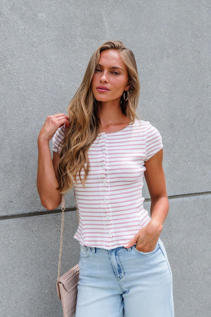Woman with long blonde hair in the Free People Stripe Most Wanted Top - Mauve and jeans, standing by a concrete wall holding a purse.
