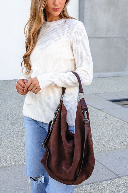 Woman outdoors holds the Free People Suzie Suede Tote Bag - Brown, wearing a white sweater and ripped jeans.