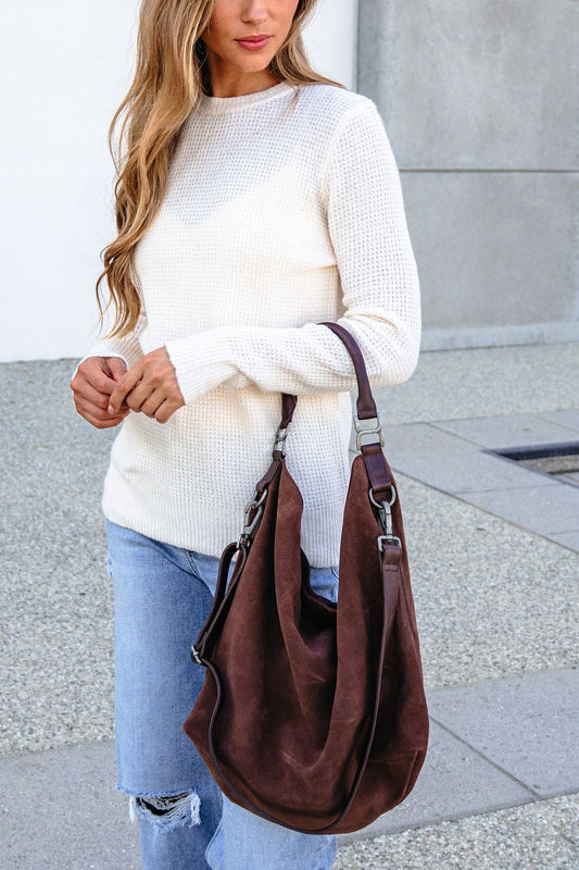 Woman outdoors holds the Free People Suzie Suede Tote Bag - Brown, wearing a white sweater and ripped jeans.