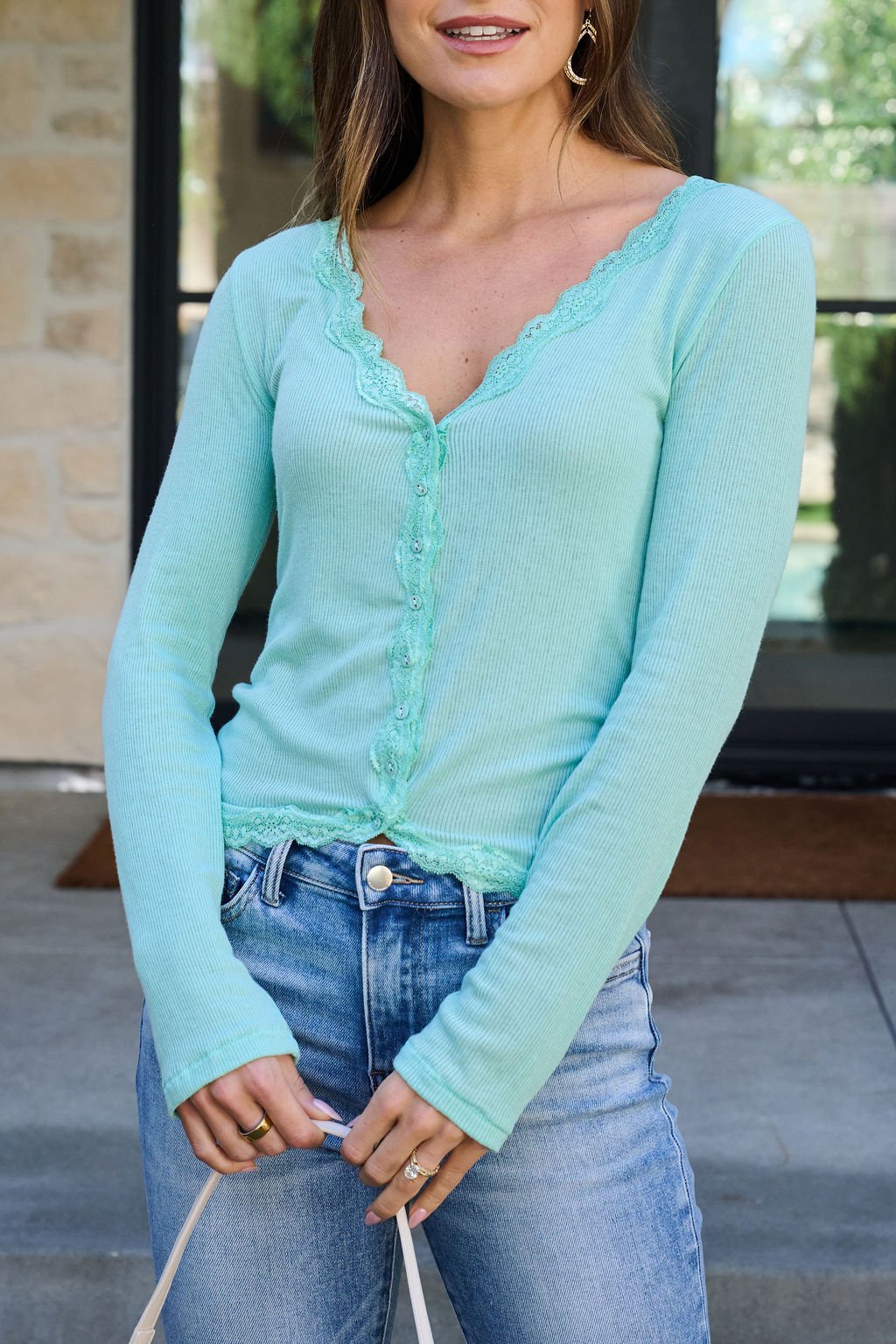 Woman in a teal Free People Big Love Ribbed Top with lace trim and blue jeans, standing outdoors before a building.
