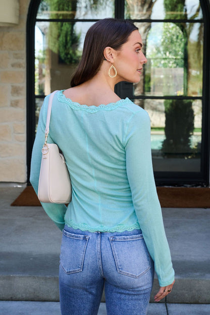 A woman in jeans stands outdoors, facing away, wearing a Free People Teal Big Love Ribbed Top and carrying a white handbag.