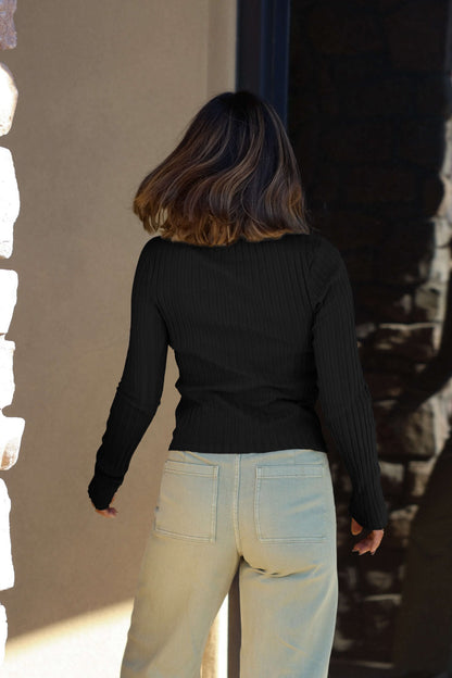 A woman wears the Free People Tilly Black Long Sleeve Top with light jeans, standing facing away from the camera.