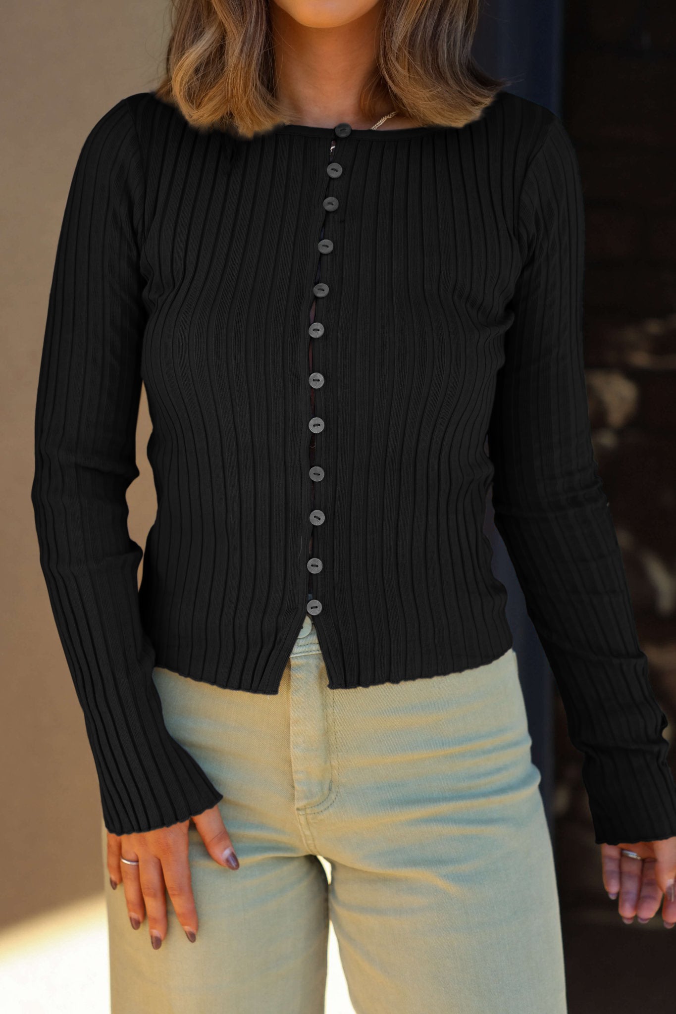 A person in the Free People Tilly Black Long Sleeve Top and light beige pants, wavy brown hair, facing forward.