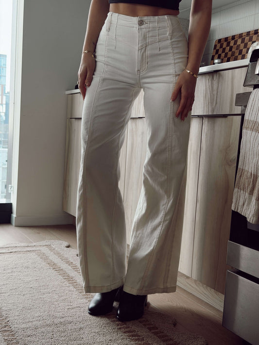 Person standing indoors wearing Free People White Libre Wide Leg Jeans, black boots, and a black top with arms relaxed.