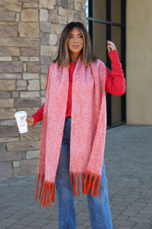 Woman outside in a red top, jeans, and the Free People Winter Chill Pink Blanket Scarf, smiling with coffee.