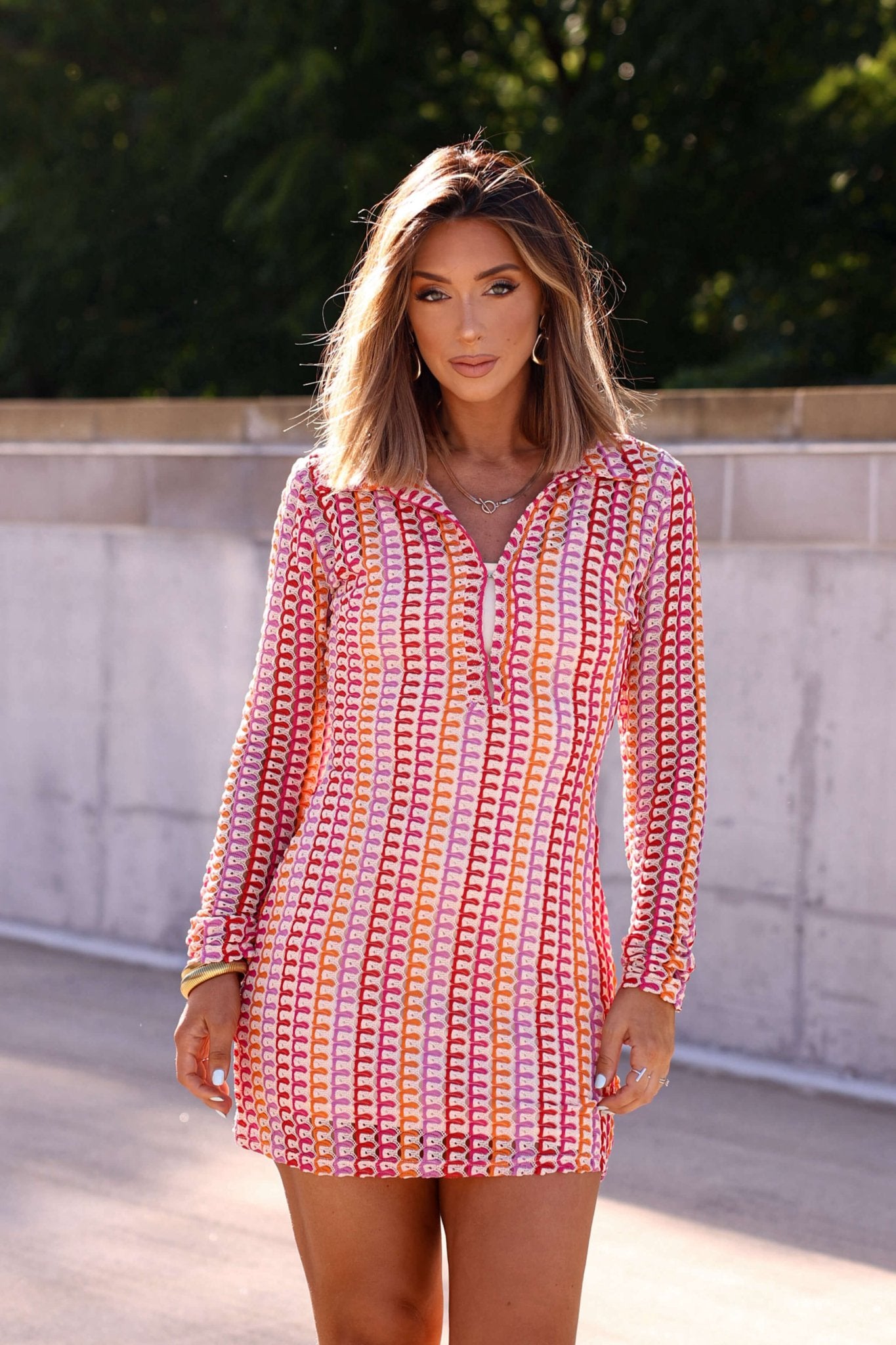 Woman wearing the Fuchsia Multi Striped Crochet Mini Dress - FINAL SALE, outdoors with trees and a concrete wall in the background.
