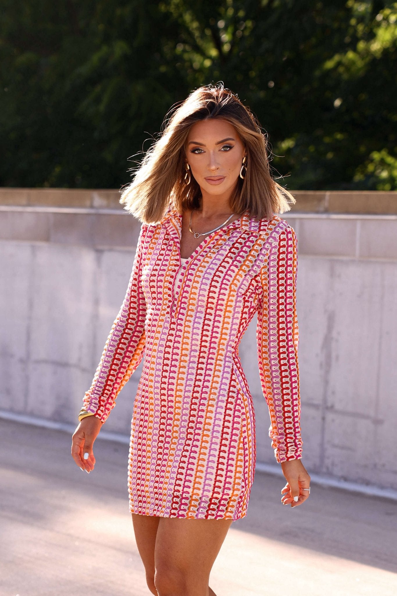 Woman in a Fuchsia Multi Striped Crochet Mini Dress - FINAL SALE stands outdoors, styling her chic mini beach cover-up.