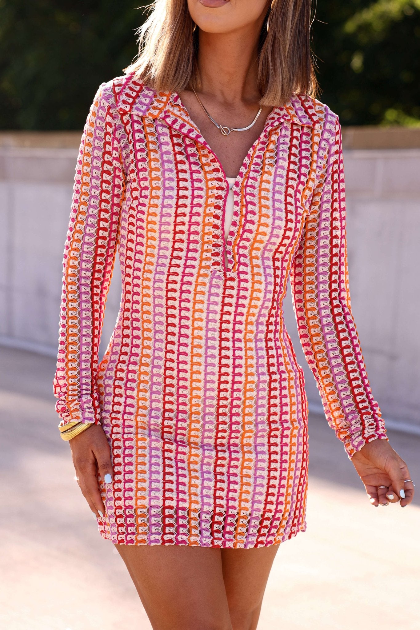 A woman stands outdoors in sunlight, wearing the Fuchsia Multi Striped Crochet Mini Dress - FINAL SALE.