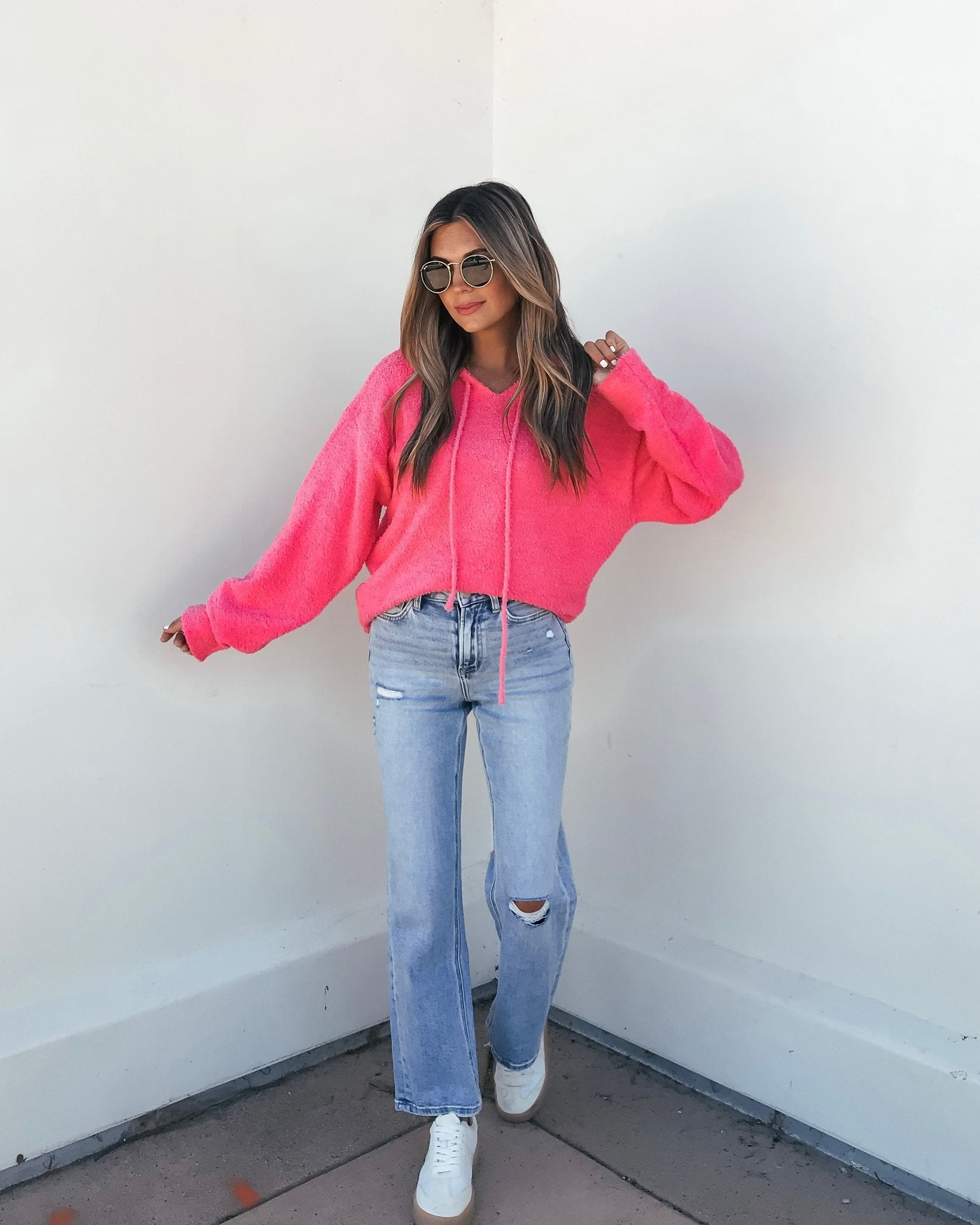 Woman styles a Fuzzy Pink Hooded Sweater with light blue ripped jeans, white sneakers, and sunglasses.