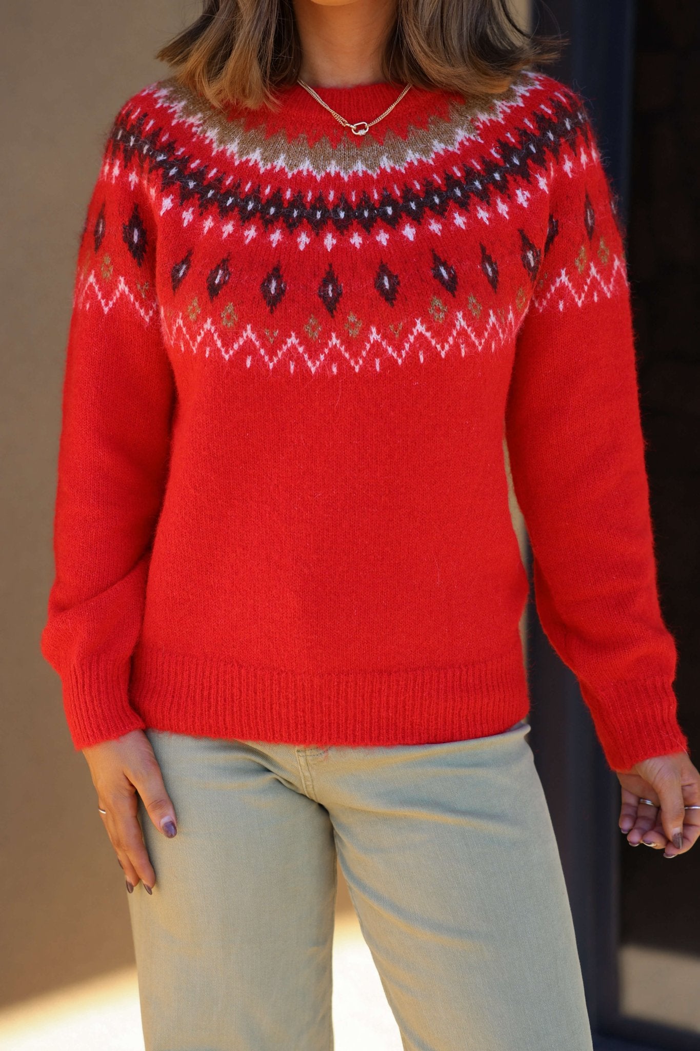 A person models the Fuzzy Red Fair Isle Crew Neck Sweater with beige pants against a neutral background.