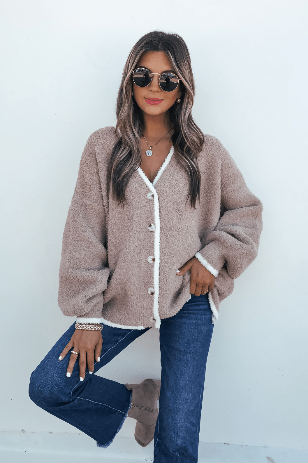Woman in sunglasses wears the Fuzzy Soft Camel Button Down Cardigan with blue jeans and taupe boots against a white background.