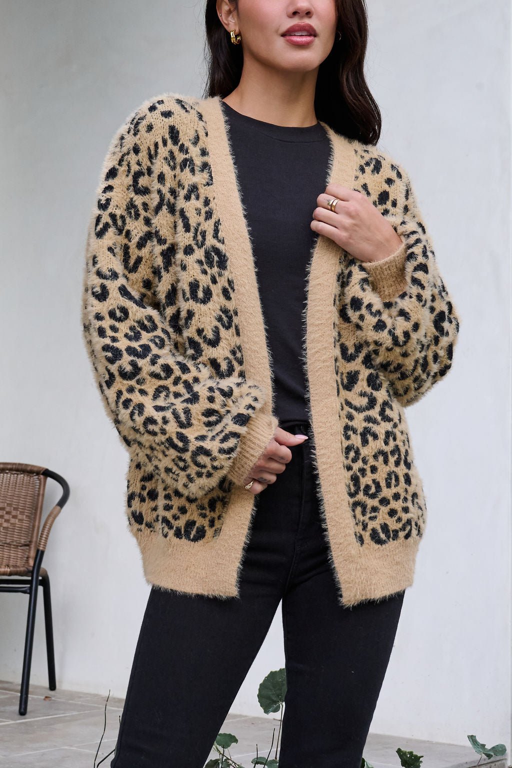 A woman wears a Fuzzy Tan Leopard Open Front Cardigan over a black shirt and pants.