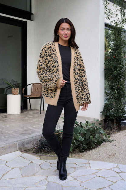 Woman outdoors in front of a house, wearing a Fuzzy Tan Leopard Open Front Cardigan, black top, black pants, and black boots.