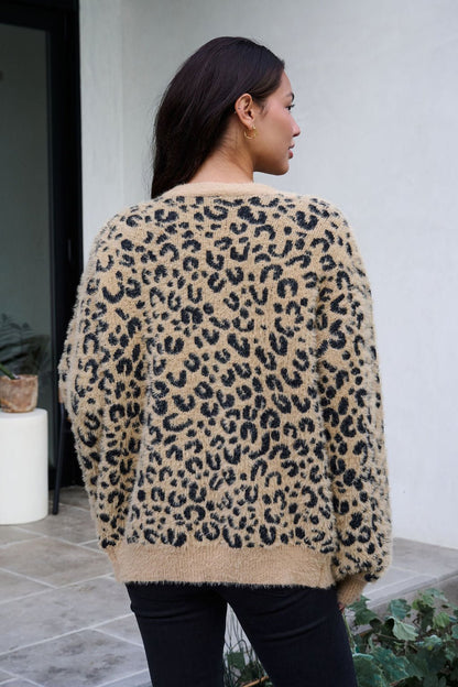 A woman with long dark hair wears the Fuzzy Tan Leopard Open Front Cardigan, standing outside and facing away from the camera.