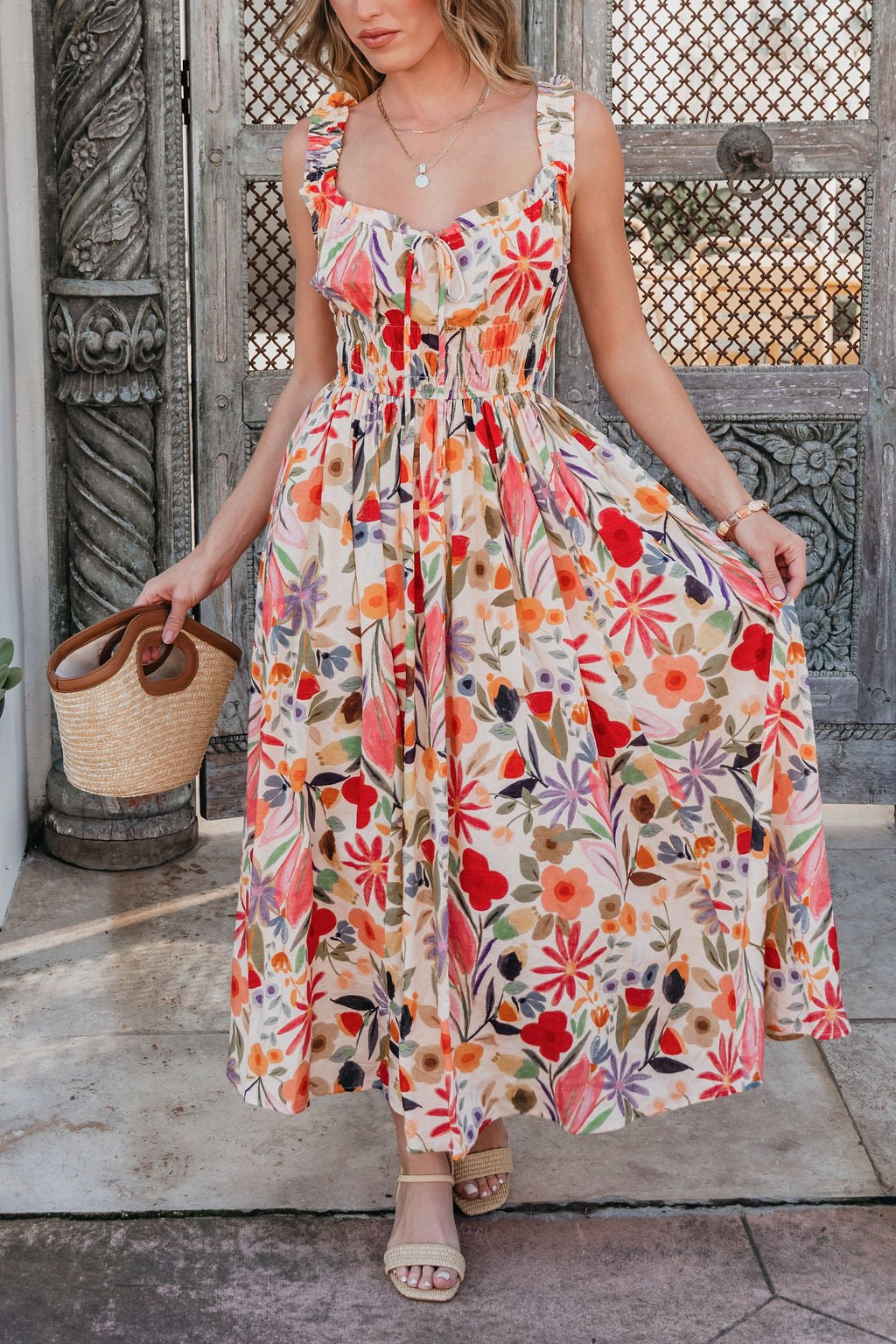 Woman in a Garden Wayfarer Print Midi Dress, holding a straw bag, stands by ornate doors in a fresh spring look.