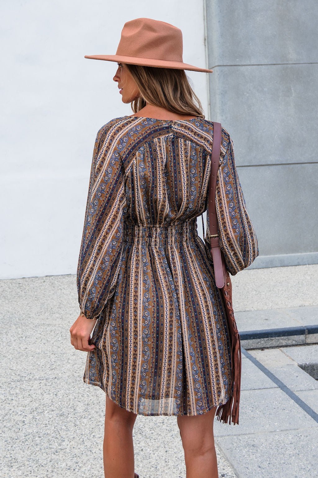 Woman in the Genevieve Floral Striped Mini Dress — Mocha stands outdoors, long balloon sleeves and a fringed bag on her shoulder.