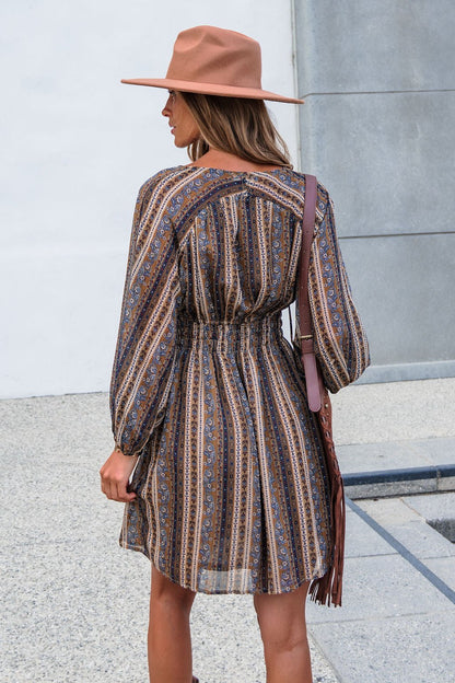 Woman in the Genevieve Floral Striped Mini Dress — Mocha stands outdoors, long balloon sleeves and a fringed bag on her shoulder.