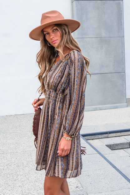 Woman wears the Genevieve Floral Striped Mini Dress—Mocha, with balloon sleeves and V-neck, standing outdoors holding a brown bag.