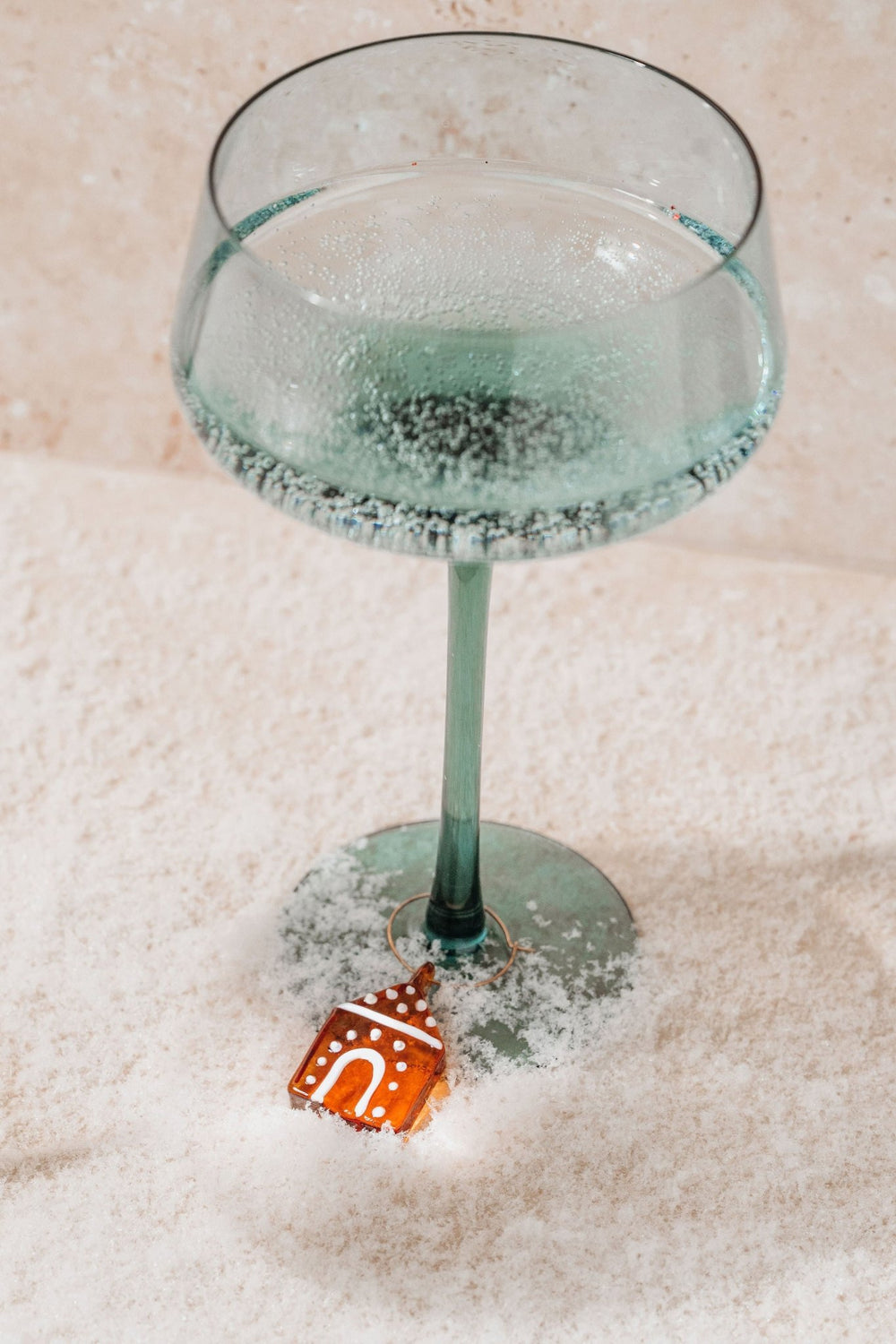 A Gingerbread Glass Wine Charm sits on snowy ground—perfect for holiday entertaining or as a charming wine gift.