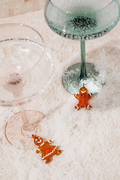 Two wine glasses with Gingerbread Glass Wine Charms and cookies on faux snow—a festive setup for holiday entertaining.