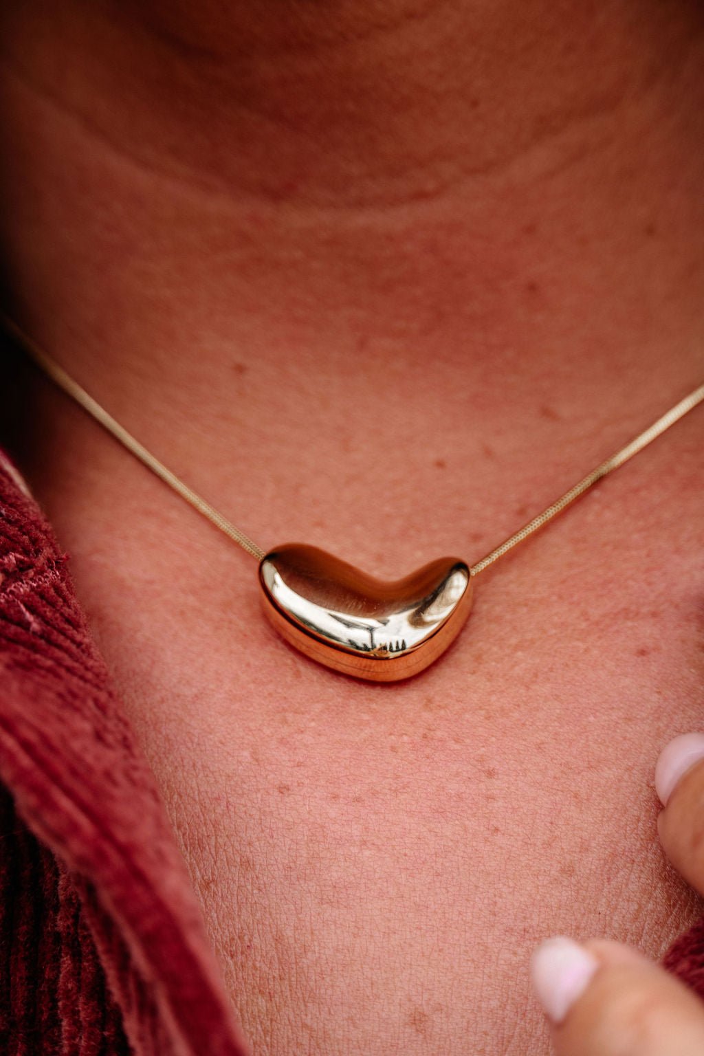 A close-up of the Gold Abstract Heart Pendant Necklace worn on the neck, paired with a red textured garment.