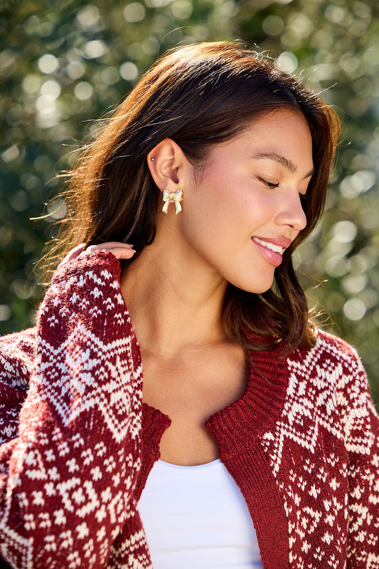 Smiling woman with long brown hair wears Gold and Pearl Bow Earrings and a red and white patterned sweater outdoors.