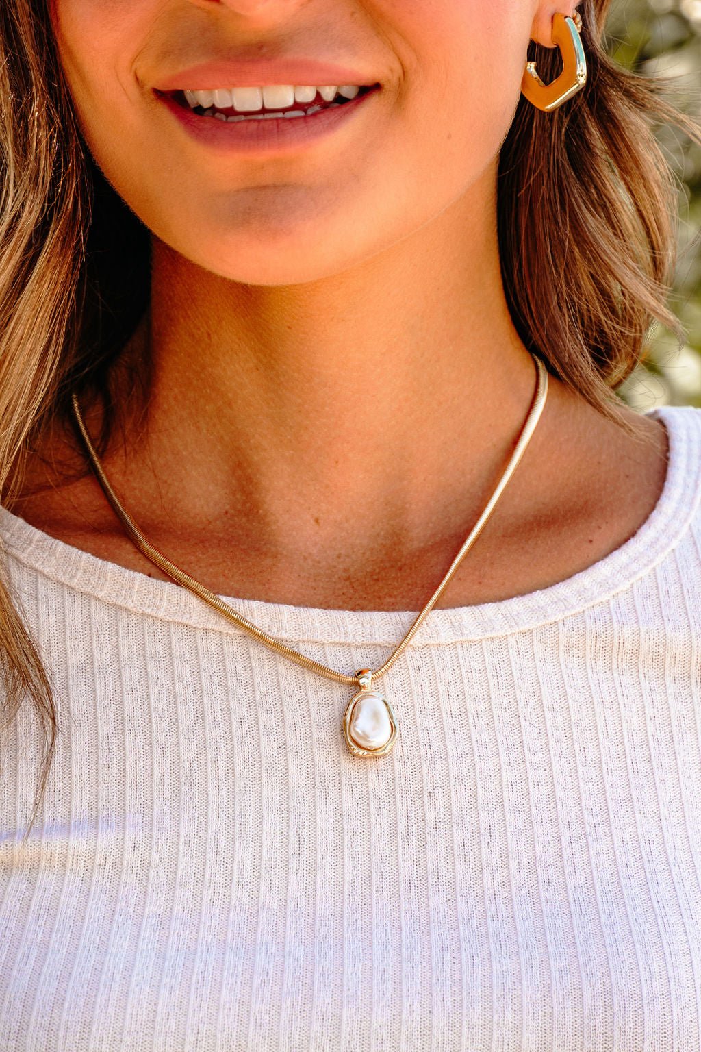 A woman wears the Gold Chain Pearl Pendant Necklace with gold hexagon earrings and a white ribbed top.