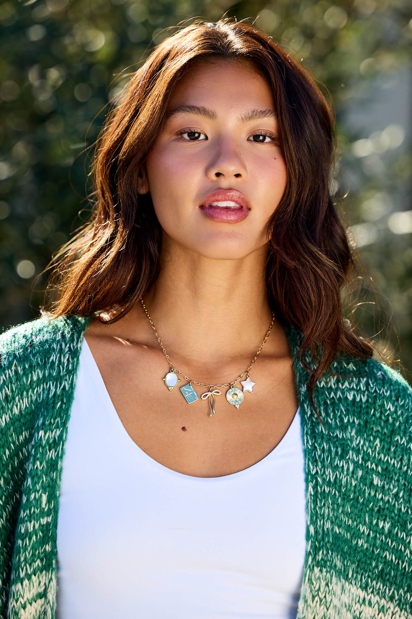 Woman with wavy brown hair in a green sweater and white top wears the Gold Christie Multi Charm Chain Link Necklace outside.