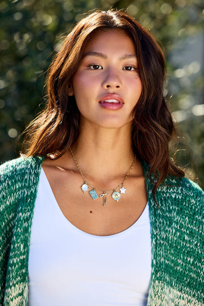 Woman with wavy brown hair in a green sweater and white top wears the Gold Christie Multi Charm Chain Link Necklace outside.