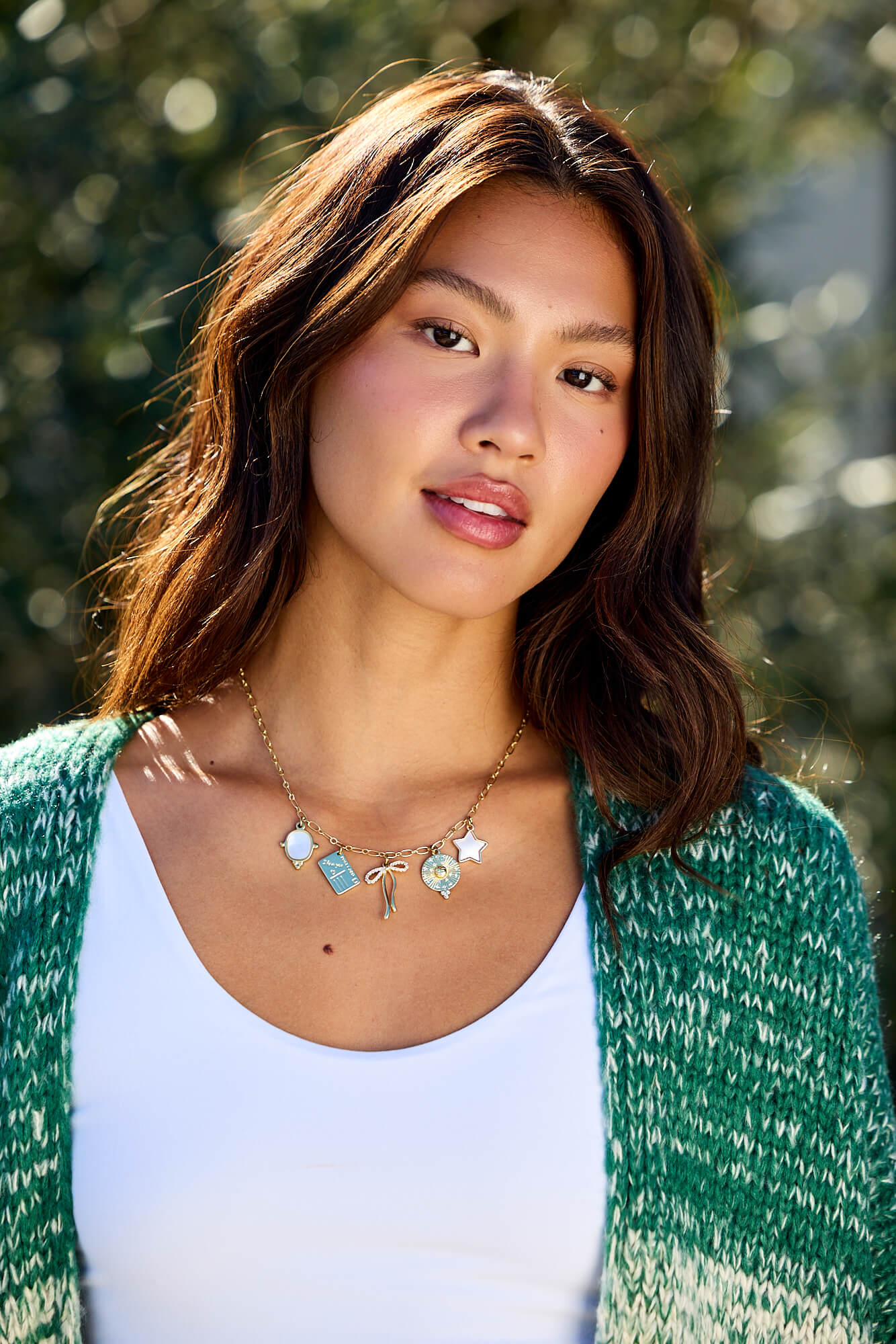 A woman wears the Gold Christie Multi Charm Chain Link Necklace outdoors, styled with a green cardigan and white top.