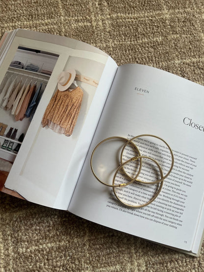 An open book with a closet photo and text displays the Gold Coiled Metallic Bracelet Set atop a beige textured surface.