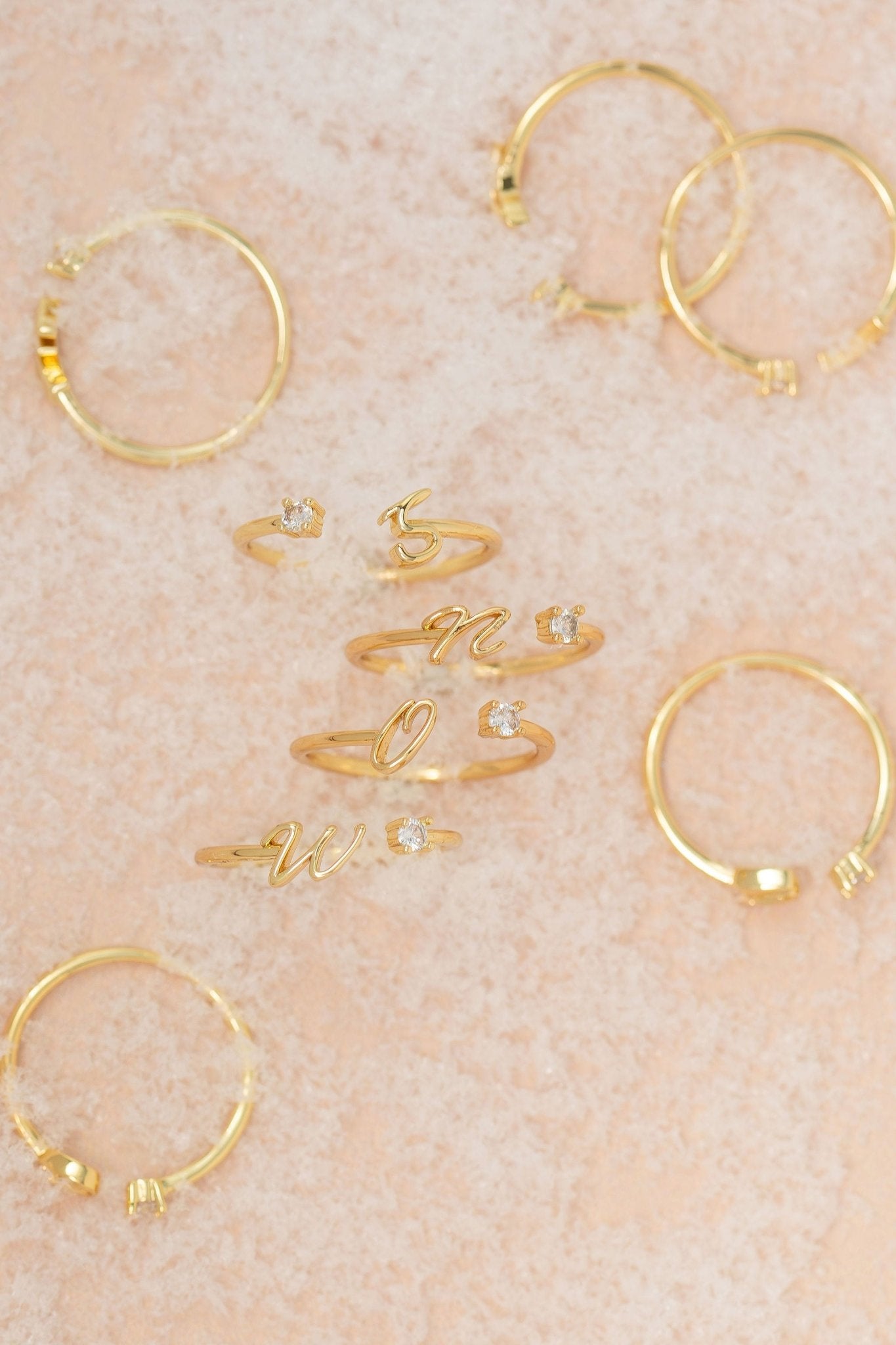 Gold Custom Initial Letter Band Ring - FINAL SALE with diamond accents shown on a light pink textured surface.