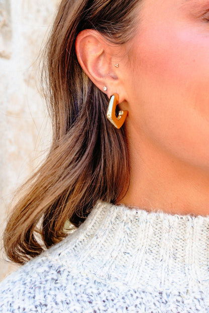 Close-up of a woman’s ear in a light knit sweater, wearing Gold Dipped Abstract Hoop Earrings and two small studs.