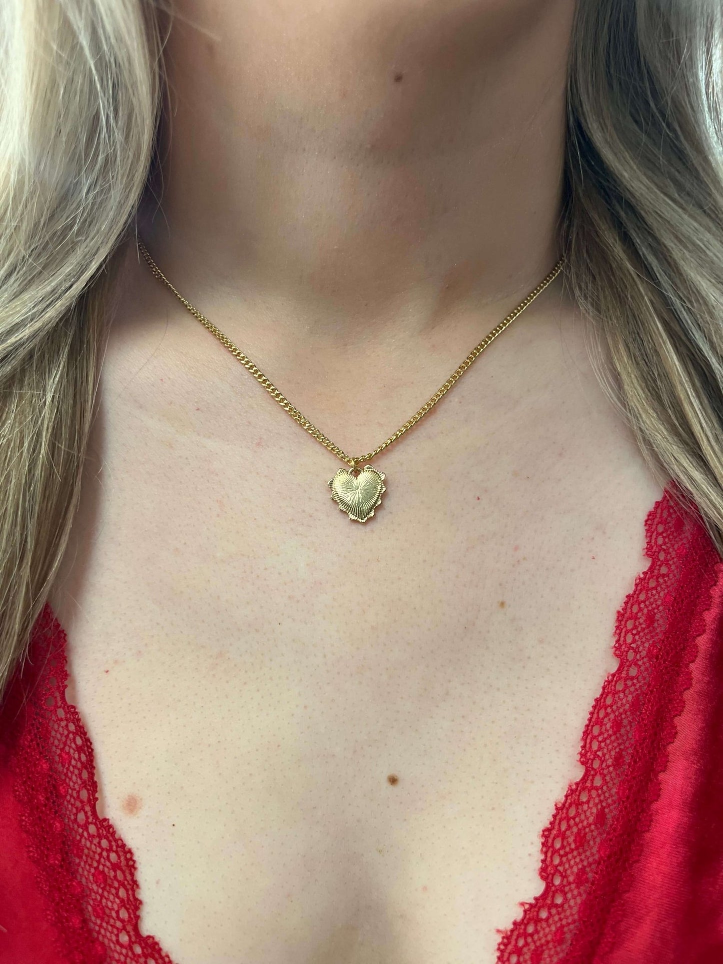 A woman wears the Gold Dipped Heart Pendant Necklace with a red lace-trimmed top.