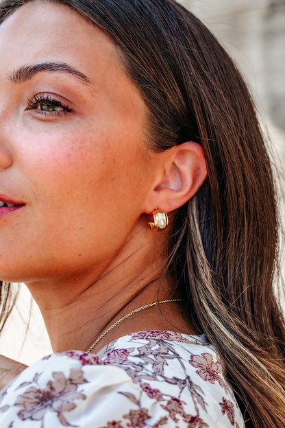 Close-up of a woman with long brown hair, wearing Gold Dipped Oval Pearl Hoop Earrings - DOORBUSTER and a floral top.