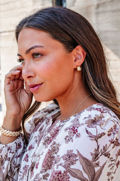 Woman in a floral blouse wears Gold Dipped Oval Pearl Hoop Earrings – DOORBUSTER, touching her face while looking to the side.