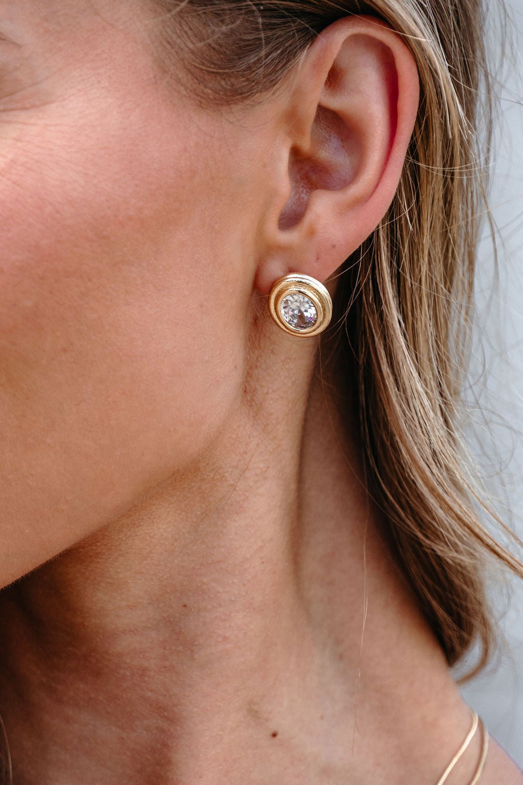 Close-up of a person wearing Gold Dipped Oval Stud Earrings, each with an elegant crystal center.